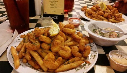 A plate of golden fried shrimp and French fries, garnished with lemon and parsley, served with dipping sauces.