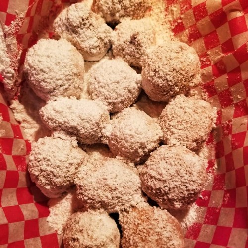 A basket lined with red and white checkered paper filled with powdered sugar-coated dough balls.