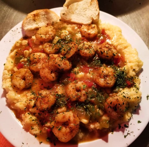 A plate of shrimp and grits topped with herbs, served with two slices of toasted bread.