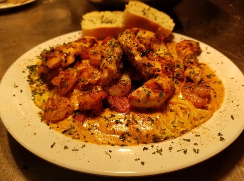 A plate of shrimp pasta topped with herbs, served with slices of garlic bread.