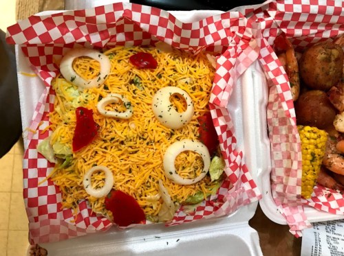 A colorful salad with shredded cheese, lettuce, sliced onions, and red peppers in a takeout container.