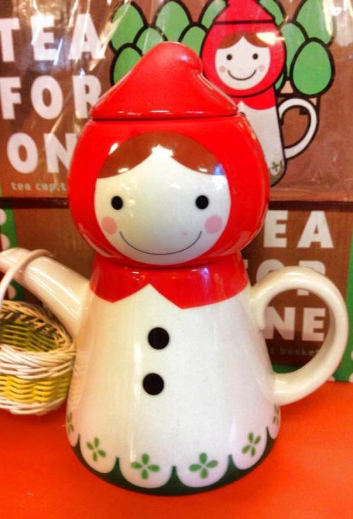 A whimsical teapot shaped like a girl in a red hood, featuring a smiling face and floral details.
