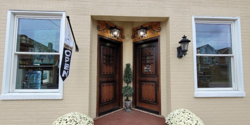 Two wooden doors with decorative lights, flanked by windows, and a sign reading "OPEN" outside a building.
