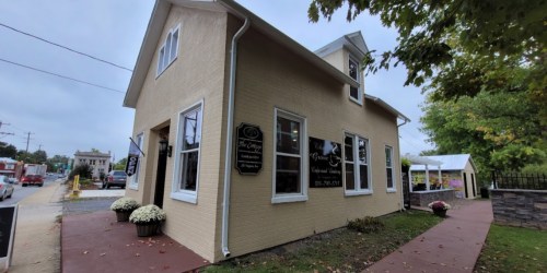 A beige building with large windows and signs, surrounded by greenery and a walkway, on a cloudy day.