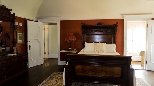 Cozy bedroom featuring a wooden bed, warm orange walls, and elegant decor, with a door leading to a bathroom.
