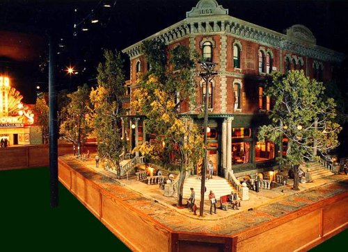 A detailed miniature model of a historic building with trees, streetlights, and small figures in a vibrant setting.
