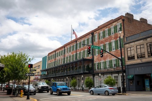Historic brick building with green shutters, American flag, and traffic lights on a busy street under a cloudy sky.