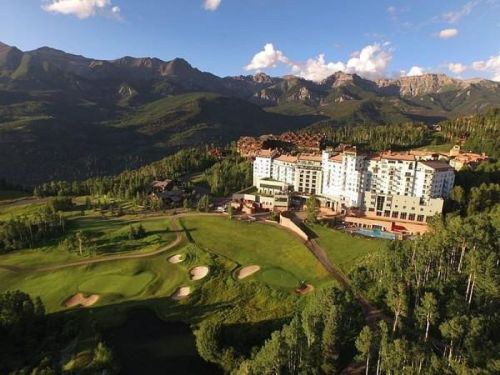 Aerial view of a luxury resort nestled in a mountainous landscape with golf courses and lush greenery.