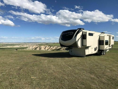 A large RV parked on a grassy area with a clear blue sky and scattered clouds in the background.
