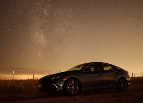 A car parked in a field under a starry night sky with the Milky Way visible in the background.