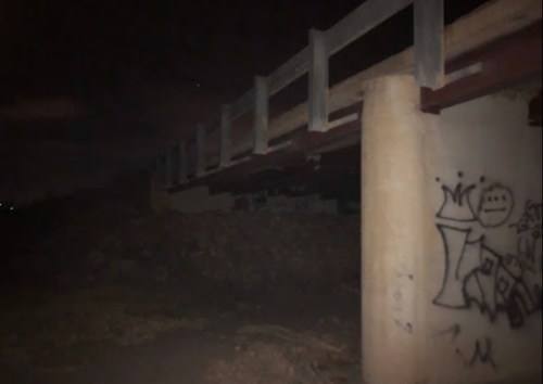 A dimly lit underpass with a concrete bridge and graffiti on the support pillar.