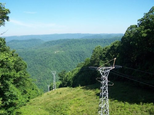 A scenic view of rolling green hills and mountains, with power lines running through the foreground under a clear blue sky.