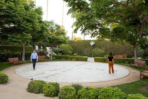 A serene garden with a circular labyrinth, featuring two people walking on the path surrounded by greenery and benches.