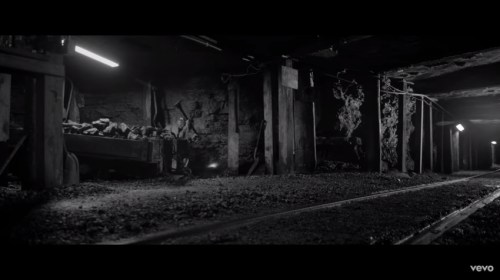 A dimly lit underground mine with tracks, wooden supports, and piles of coal, creating a moody, industrial atmosphere.