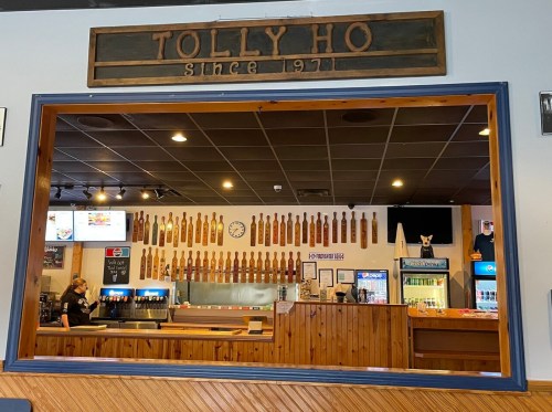 Interior view of Tolly Ho restaurant, featuring a bar with numerous beer taps and a staff member serving customers.