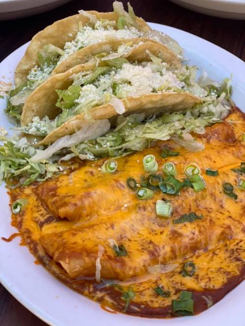 A plate featuring cheesy enchiladas topped with green onions, alongside tacos filled with lettuce and cheese.