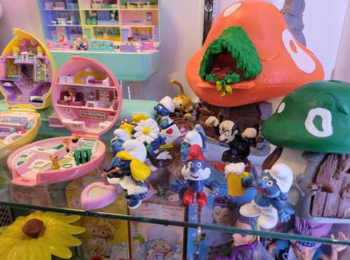 Colorful display of toy figures, including Smurfs and a mushroom house, alongside miniature playsets and flowers.