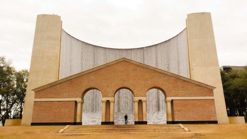A large, modern building with a curved wall and brick facade, featuring arched entrances and a person standing in front.