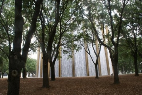 A serene park scene featuring tall trees surrounding a large, cascading waterfall structure.