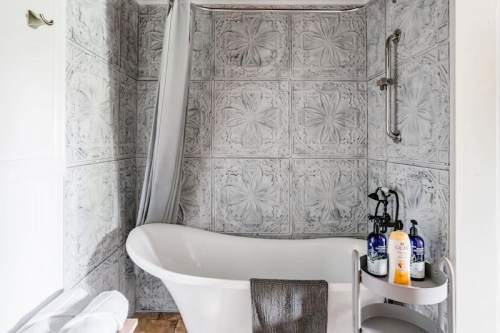 A modern bathroom featuring a freestanding bathtub, textured wall tiles, and a small shelf with toiletries.