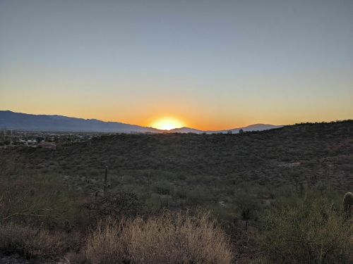A serene sunset over rolling hills, with a clear sky and distant mountains in the background.