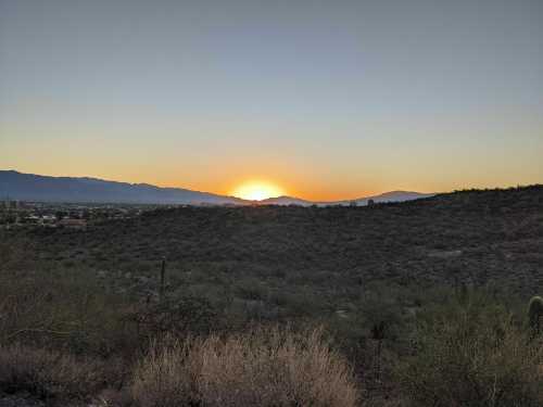 A serene sunset over rolling hills, with a clear sky and distant mountains in the background.