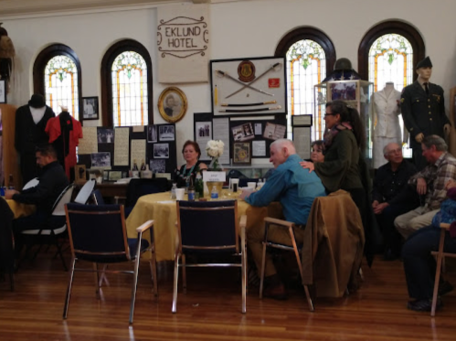A group of people seated at tables in a museum, surrounded by historical displays and artifacts.