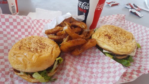 Two sesame seed burgers with lettuce, accompanied by a side of onion rings and a Coca-Cola drink.