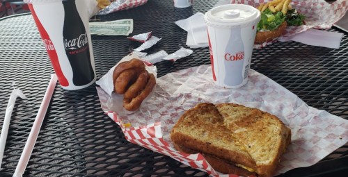 A table with fast food items: a sandwich, onion rings, and drinks in Coca-Cola cups on a checkered paper.