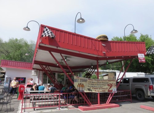 A red and white diner with a unique roof design, featuring outdoor seating and a menu sign. Customers are dining outside.