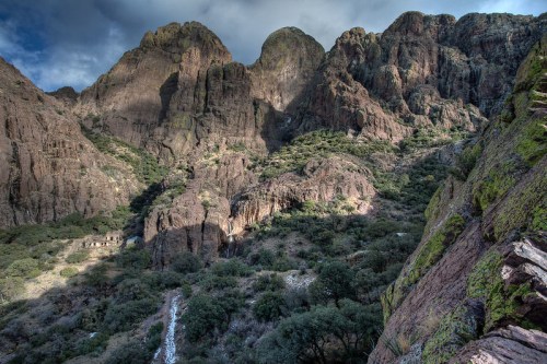 A dramatic landscape featuring rugged mountains and a lush valley under a cloudy sky.