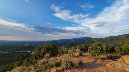 Panoramic view of rolling hills and valleys under a blue sky with scattered clouds, showcasing lush greenery.