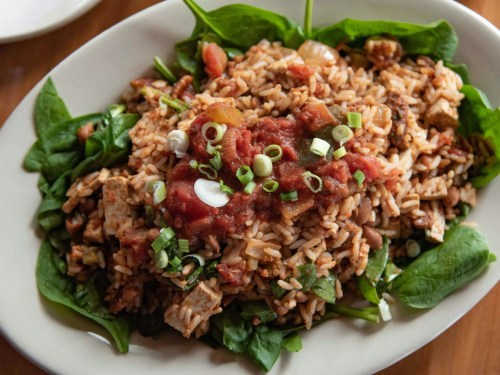 A bowl of rice mixed with vegetables and topped with salsa and green onions, served on a bed of fresh spinach.