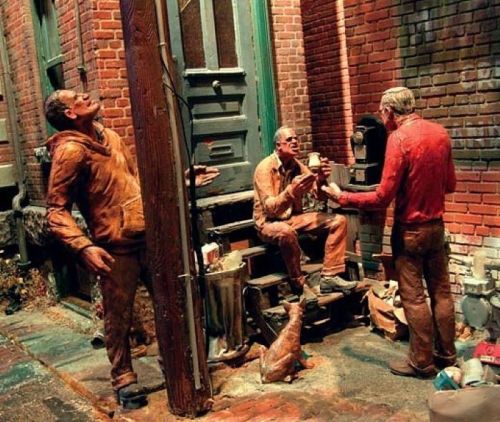 Three life-like sculptures of men interacting in a brick alley, with a dog nearby and vintage elements in the scene.