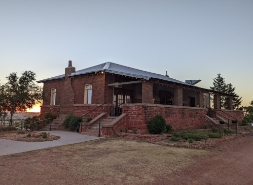 A brick house with a porch, surrounded by trees, at sunset, showcasing a warm, inviting atmosphere.