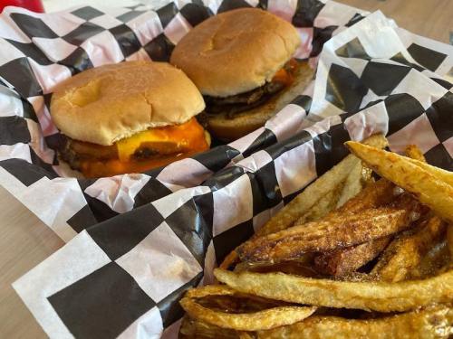 Two cheeseburgers in a basket with black and white checkered paper, alongside a serving of golden fries.