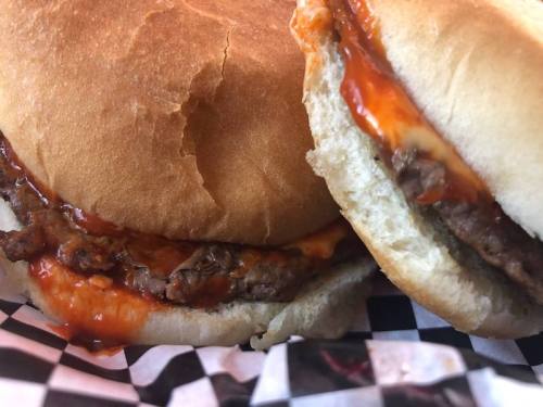 Close-up of two hamburger sandwiches with meat and sauce on a checkered paper background.