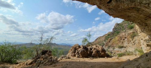 A scenic view from a cave opening, showcasing mountains and a blue sky with scattered clouds.