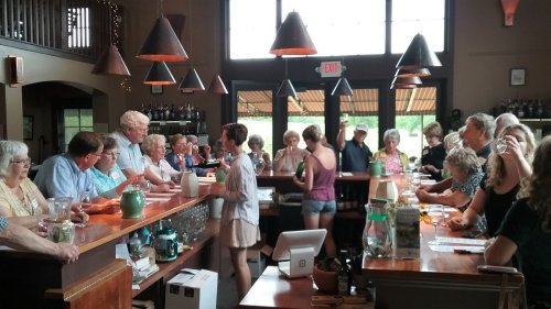 A busy bar scene with a diverse group of people socializing and enjoying drinks at a wooden counter.