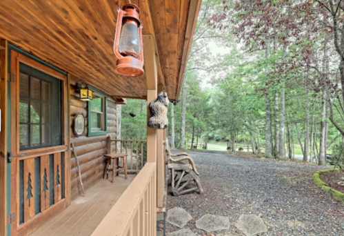 A rustic cabin porch with a lantern, wooden decor, and a gravel path surrounded by trees.