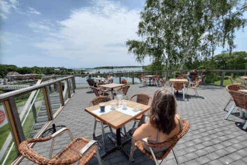 A scenic outdoor dining area with tables overlooking a water view, featuring people enjoying their meals.