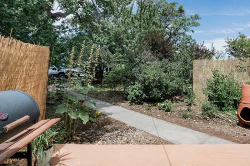 A garden path surrounded by greenery, with a grill and decorative fencing in the foreground.