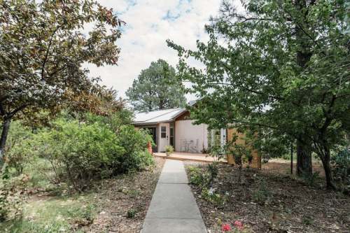 A pathway leads to a cozy house surrounded by trees and greenery under a partly cloudy sky.