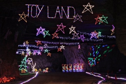 Colorful holiday lights spell "Toy Land" and feature stars, a dinosaur, and festive figures in a cave setting.