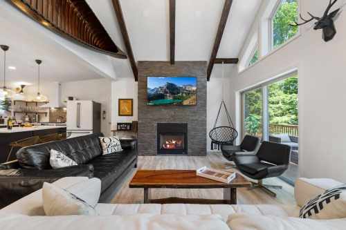 Modern living room with a fireplace, large windows, and a TV mounted on the wall, featuring stylish furniture and decor.
