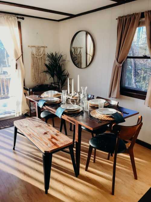 A cozy dining room with a wooden table set for a meal, featuring candles, glassware, and a decorative mirror.