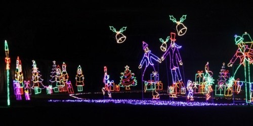 Colorful holiday light display featuring trees, gifts, and festive figures against a dark background.