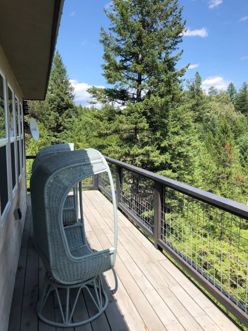 A cozy balcony with two wicker chairs overlooking a lush green forest and blue sky.