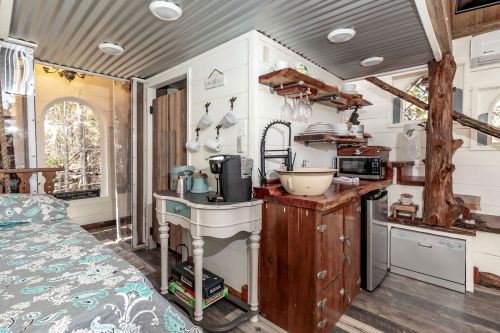 Cozy interior of a tiny home featuring a kitchenette, wooden shelves, and a staircase leading to a loft.