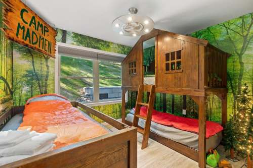A cozy bedroom with a treehouse bed, colorful bedding, and a forest-themed mural on the walls.